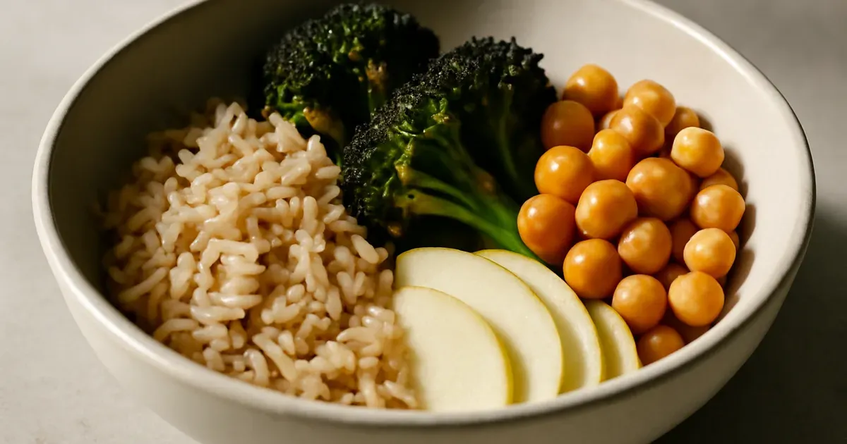 Balanced high-fiber meal bowl with brown rice, chickpeas, roasted broccoli, and sliced apple on a stone surface